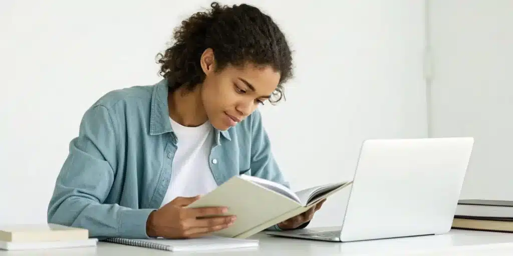 How to Focus on Reading for School & Learn Faster 6 A student learns how to focus on reading for school, studying a book at a desk with a laptop.